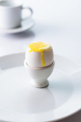 Soft boiled egg in egg cup on white background, plate and cup. Close up. Selective focus. Vertical shot.