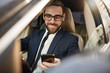 © AnnaStills - Successful young businessman in eyeglasses reading a message on his mobile phone and smiling in his car