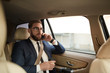 © AnnaStills - Worried young businessman talking on mobile phone and drinking coffee while sitting on back seat of a taxi
