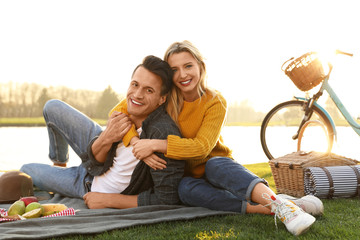 Happy young couple having picnic near lake on sunny day