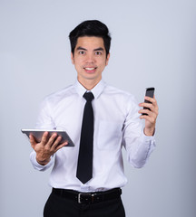 Portrait handsome young asian man wearing a white shirt holding smart phone or tablet smile and happy isolated on gray background in studio. Asian man people. business success concept.