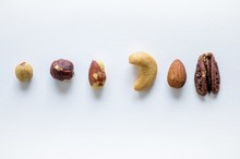 Overhead Shot Of Different Nuts In A Line On A White Surface