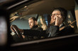 © AnnaStills - Young bearded driver in eyeglasses using his mobile phone during driving with passenger sitting near by him
