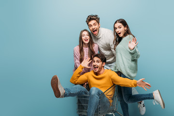 laughing friends having fun with shopping cart, isolated on blue