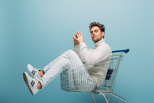 Handsome Pensive Man Sitting In Shopping Cart, Isolated On Blue