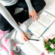 Woman studying Bible on white bed. With open laptop, journal, pen, Bible notes and pink flowers