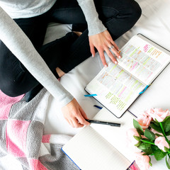 Wall Mural - Woman studying Bible on white bed. With open laptop, journal, pen, Bible notes and pink flowers