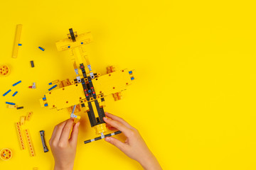 Child hands making construction plane over yellow background. Robotic, learning, technology, stem education for children background