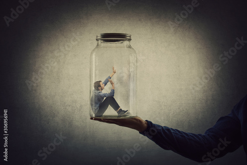 Cuadros en Lienzo Business concept with a scared tiny man trapped inside a glass jar held by his gigantic boss hand