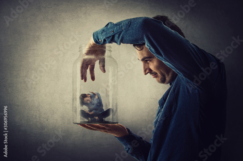 Fotografía Conceptual scene, scared tiny boy trapped inside a glass jar held in hand by a scary giant