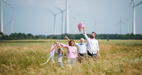 Wall Mural - Multigeneration family standing on field on wind farm, playing with kite.