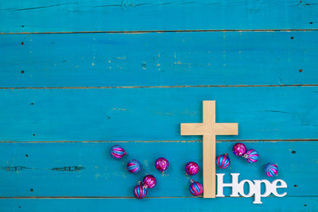 Wall Mural - Wood cross with the word Hope hanging on antique rustic teal blue wooden background with colorful turquoise and pink Christmas ornaments; religious holiday and spiritual background with copy space