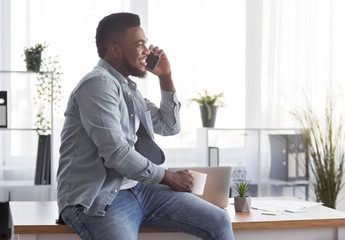 Poster - Smiling employee resting in office, sitting on desk with coffee and cellphone