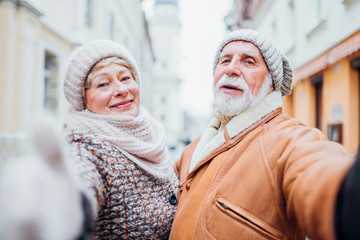 Tourism and technology. Positive smiling senior couple wearing warm clothes taking a selfie together enjoying life against the background of attractions of old city