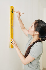 Poster - Pretty young Asian woman using spirit level for drawing horizontal line on the wall in her new house