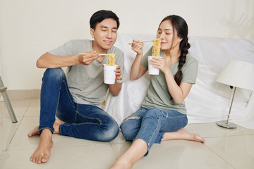 Poster - Hungry young Asian couple enjoying smell of instant noodle they are having for lunch after moving in new apartment