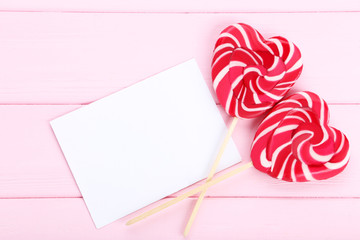 Wall Mural - Heart shaped lollipops with blank sheet of paper on pink wooden table