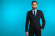 Copy space. Portrait of young successful confident businessman with beard isolated on blue studio background. Man in business suit looking to camera and smiling. Portraiture of handsome guy.