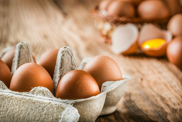 Wall Mural - Eggs on wooden table. Brown eggs in wood basket. Chicken eggs in carton box. Fresh.  Broken Egg with yolk in background.