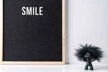The Word Smile On Black Letter Board With Happy Troll On White Desk. Interior And Word Concept.