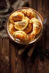 Wall Mural - Baked dumplings (pierogi) with mushroom stuffing in a ceramic bowl on a wooden table, top view. Vegetarian dish