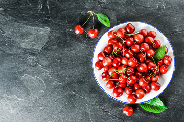 Wall Mural - Fresh red cherries in white plate top view. Pair of cherry on dark stone or black background.