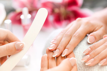 Wall Mural - Woman beautician using  a nail file. Professional and beautiful hands with nails care manicure applying in luxury salon. Pink red flowers background.