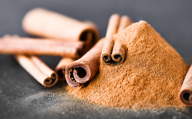 Cinnamon sticks spices on dark stone table. Cinnamons milled powder in white bowl on black board.