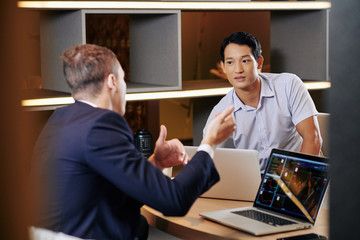 Young Vietnamese businessman listening to his colleague talking about company development and investment strategy