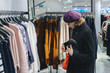 Beautiful French woman wearing purple beret hat looking at the orange leather purse in fashionable clothing store