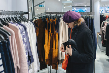 Beautiful French woman wearing purple beret hat looking at the orange leather purse in fashionable clothing store