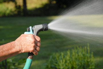 Woman spraying a hose, nozzle spraying water, watering the garden