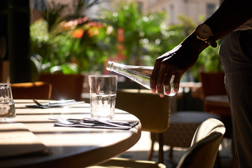 Wall Mural - Man with watch on his wrist is pouring fresh water to the glass.