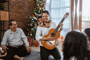 Wall Mural - family and friend singing a song together. father playing guitar during christmas