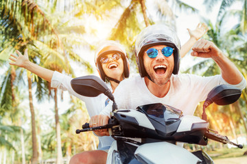 happy smiling couple travelers riding motorbike scooter in safety helmets during tropical vacation u