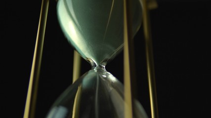 Wall Mural - Hourglass clock time concept. Old vintage gold metal frame green sand clock countdown on dark background. Close up.