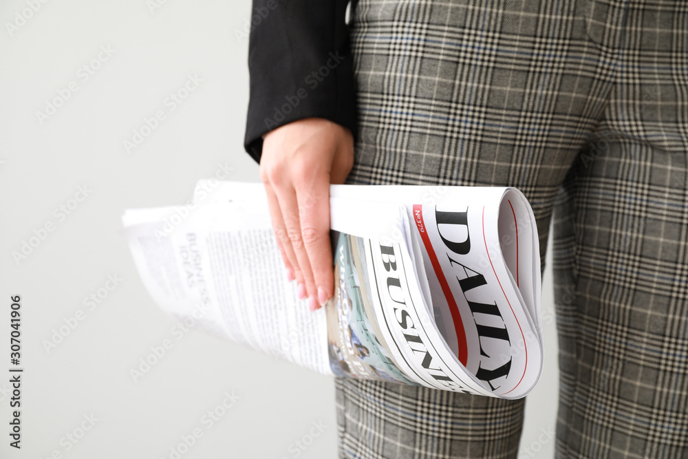 Young businesswoman with newspaper on light background, closeup