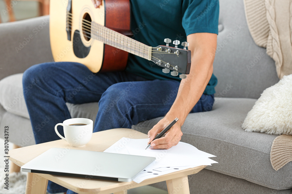Handsome man with guitar composing music at home