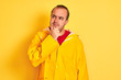 © Krakenimages.com - Young man wearing rain coat standing over isolated yellow background with hand on chin thinking about question, pensive expression. Smiling with thoughtful face. Doubt concept.