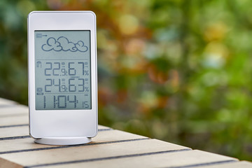 Wall Mural - Best personal weather station device with weather conditions inside and outside on foliage background. Home digital weather forecast concept with temperature and humidity.