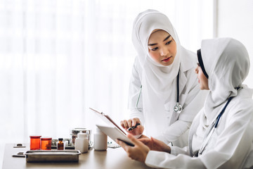 Wall Mural - Two muslim asian female doctor working with clipboard and tablet computer on desk in hospital.healthcare and medicine