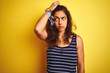 © Krakenimages.com - Young beautiful woman wearing striped t-shirt standing over isolated yellow background confuse and wondering about question. Uncertain with doubt, thinking with hand on head. Pensive concept.