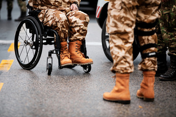 Details with a Romanian army veteran soldier, injured and disabled, sitting in a wheelchair dressed in his military desert camouflage uniform.