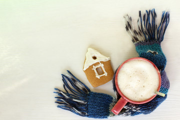 Wall Mural - red mug with foamy cappuccino and ginger house, scarf and on a table top view. cozy coffee pause