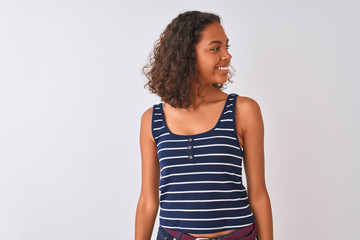 Wall Mural - Young brazilian woman wearing striped t-shirt standing over isolated white background looking away to side with smile on face, natural expression. Laughing confident.