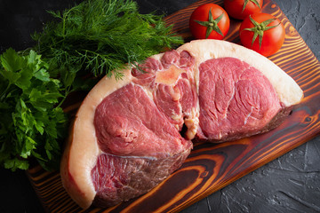 A large piece of raw horse meat on a dark background with fresh vegetables