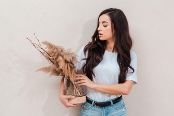 beautiful girl holding a condemned composition of grass, admiring it on a beige background