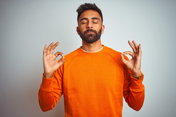 Wall Mural - Young indian man wearing orange sweater over isolated white background relax and smiling with eyes closed doing meditation gesture with fingers. Yoga concept.