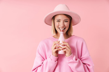 Poster - Portrait of optimistic woman in hat smiling while drinking from bottle