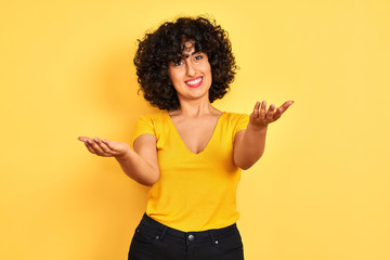 Sticker - Young arab woman with curly hair wearing t-shirt standing over isolated yellow background smiling cheerful offering hands giving assistance and acceptance.